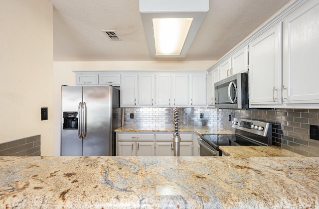 kitchen with white cabinets, appliances with stainless steel finishes, backsplash, and light stone counters