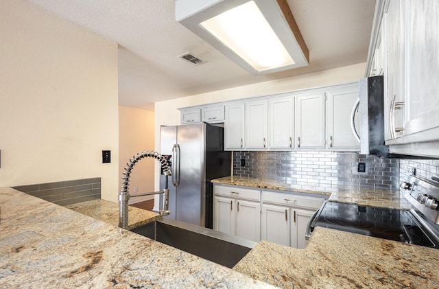 kitchen with white cabinets, light stone countertops, backsplash, and appliances with stainless steel finishes