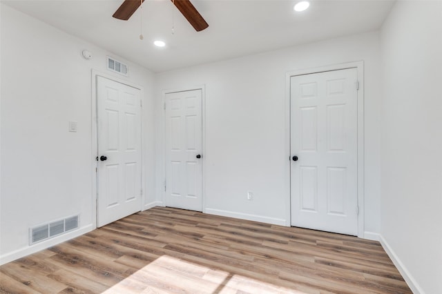 unfurnished bedroom featuring ceiling fan, two closets, and hardwood / wood-style flooring