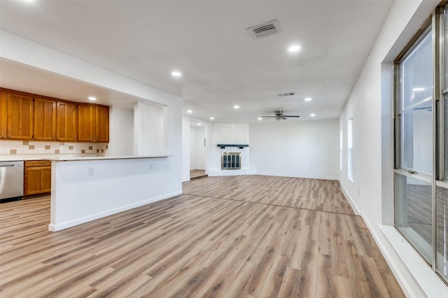 kitchen with stainless steel dishwasher, decorative backsplash, ceiling fan, light wood-type flooring, and a fireplace