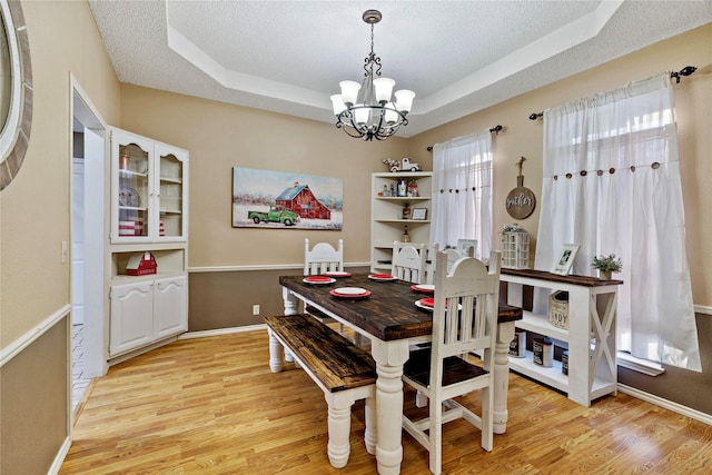 dining area featuring light hardwood / wood-style flooring, an inviting chandelier, a textured ceiling, and a tray ceiling