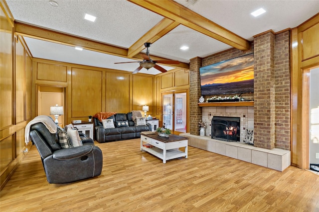 living room featuring ceiling fan, light hardwood / wood-style flooring, beamed ceiling, a textured ceiling, and a fireplace