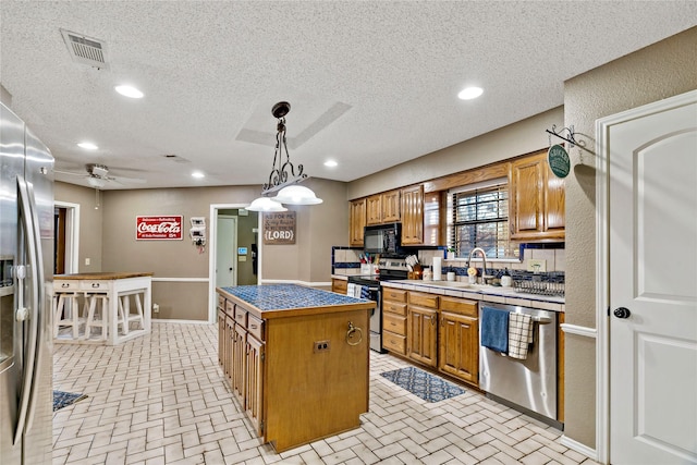 kitchen with a textured ceiling, stainless steel appliances, ceiling fan, a kitchen island, and hanging light fixtures