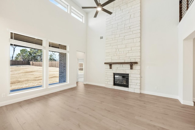 unfurnished living room featuring ceiling fan, a fireplace, baseboards, and wood finished floors