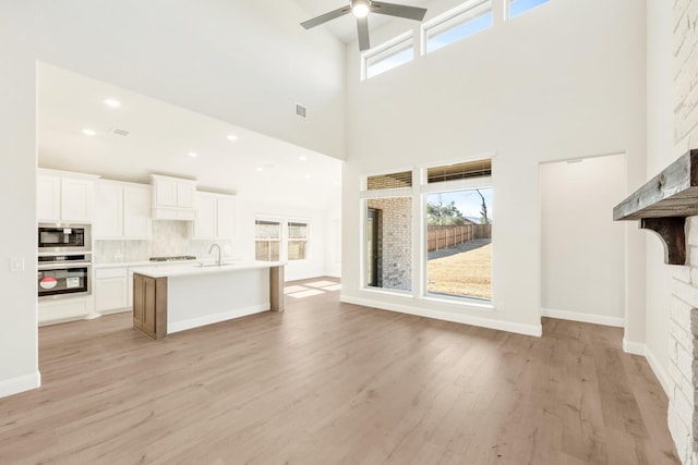 kitchen featuring a fireplace, stainless steel appliances, decorative backsplash, ceiling fan, and light wood-type flooring