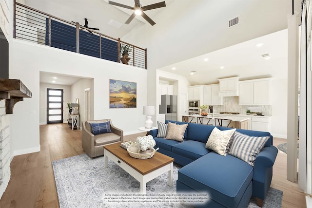 living area with visible vents, high vaulted ceiling, and light wood-type flooring