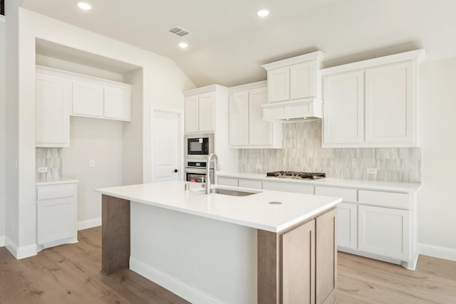 kitchen featuring a kitchen island with sink, stainless steel appliances, a sink, white cabinetry, and backsplash