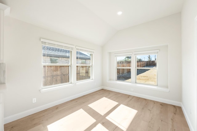 unfurnished room featuring a wealth of natural light, vaulted ceiling, baseboards, and wood finished floors