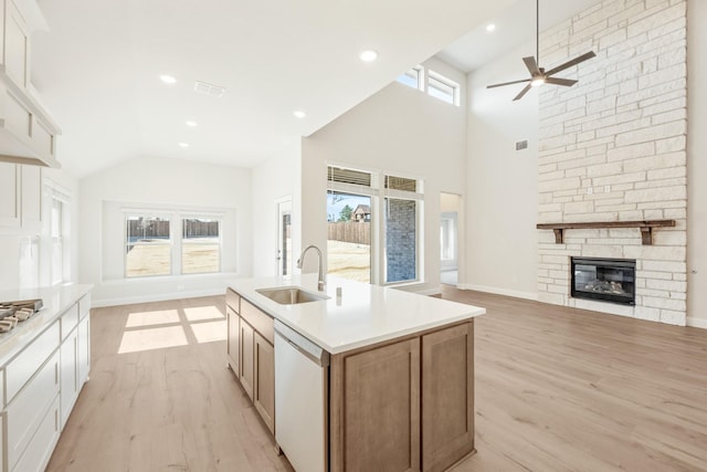 kitchen with white dishwasher, a fireplace, a sink, open floor plan, and light wood-type flooring