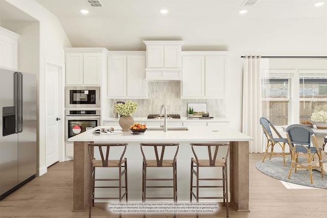 kitchen with backsplash, light countertops, white cabinets, stainless steel appliances, and a kitchen island with sink