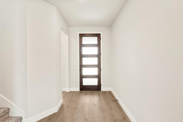 doorway to outside featuring baseboards, light wood-style floors, and stairs