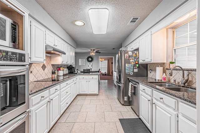 kitchen featuring stainless steel appliances, decorative backsplash, dark stone countertops, white cabinets, and sink