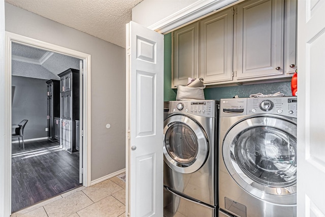 laundry area with a textured ceiling, light tile patterned flooring, washing machine and clothes dryer, and cabinets