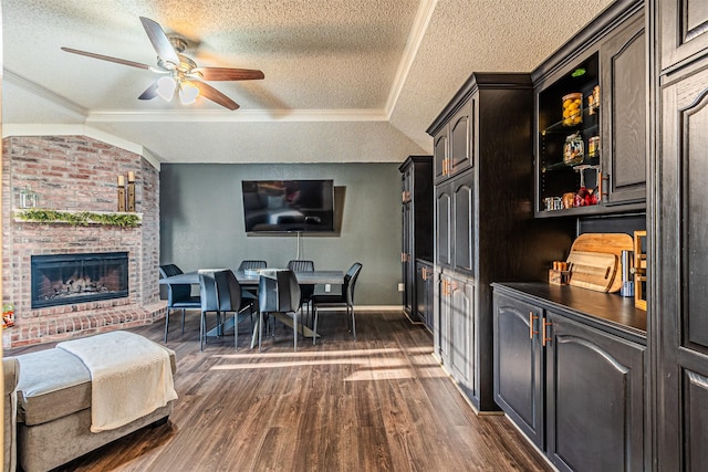 dining room featuring lofted ceiling, ceiling fan, a brick fireplace, crown molding, and dark wood-type flooring