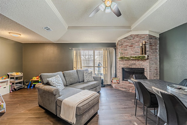 living area with visible vents, a ceiling fan, a textured wall, wood finished floors, and a brick fireplace