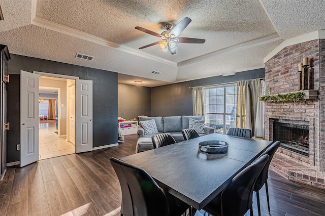 dining area with ceiling fan, a tray ceiling, dark hardwood / wood-style flooring, a fireplace, and a textured ceiling