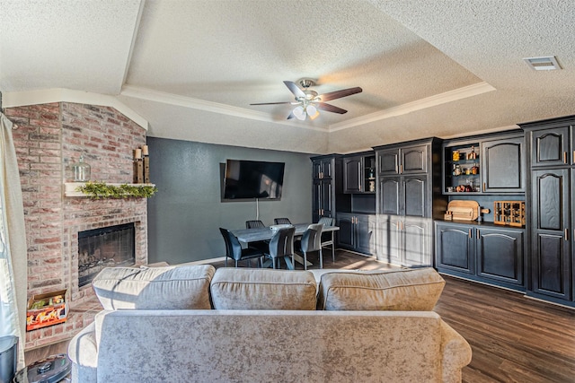 living area featuring a fireplace, visible vents, dark wood finished floors, a ceiling fan, and a raised ceiling