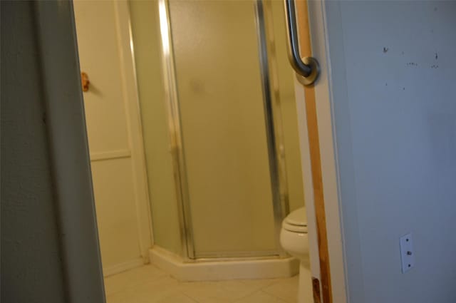 bathroom with toilet, tile patterned floors, and a shower with door