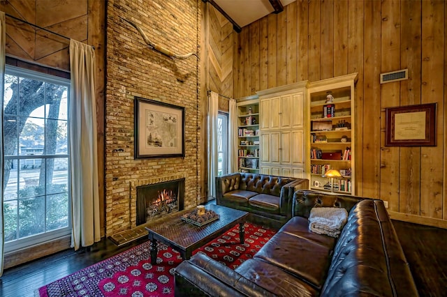 living room with a brick fireplace, a towering ceiling, dark wood-type flooring, and wood walls