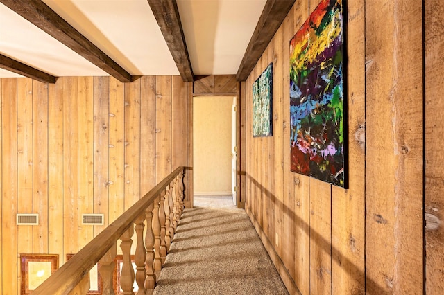 hallway with beamed ceiling, carpet floors, and wood walls