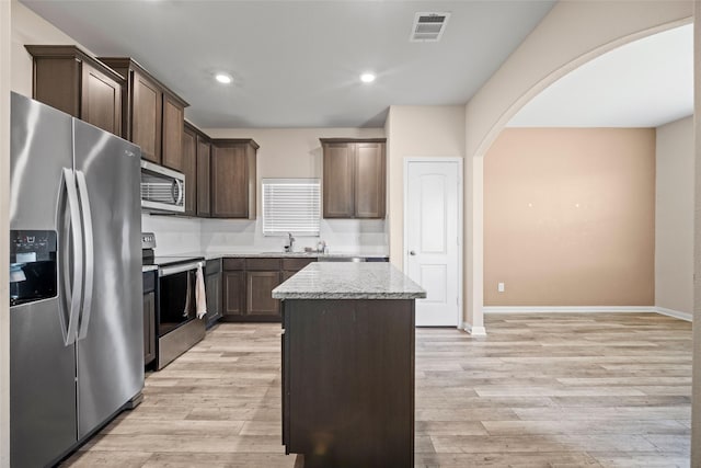 kitchen with light stone countertops, a center island, light wood-type flooring, and appliances with stainless steel finishes