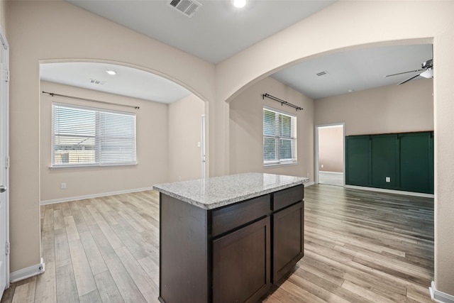 kitchen with dark brown cabinetry, ceiling fan, a center island, light stone counters, and light wood-type flooring