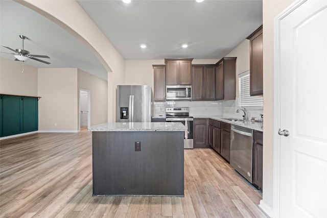 kitchen featuring ceiling fan, decorative backsplash, light stone countertops, appliances with stainless steel finishes, and a kitchen island