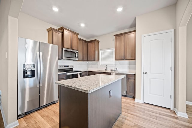 kitchen with light stone counters, light hardwood / wood-style flooring, a kitchen island, and stainless steel appliances