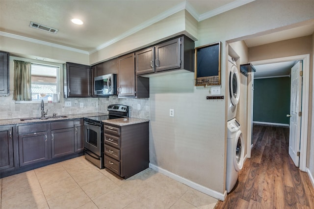 kitchen with sink, ornamental molding, stacked washer / drying machine, light stone counters, and stainless steel appliances