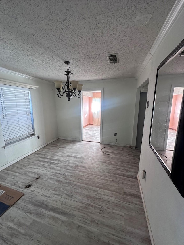 unfurnished dining area featuring a chandelier, hardwood / wood-style floors, a textured ceiling, and ornamental molding