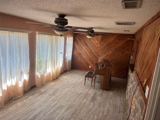 unfurnished room featuring wooden walls, hardwood / wood-style floors, ceiling fan, and a textured ceiling