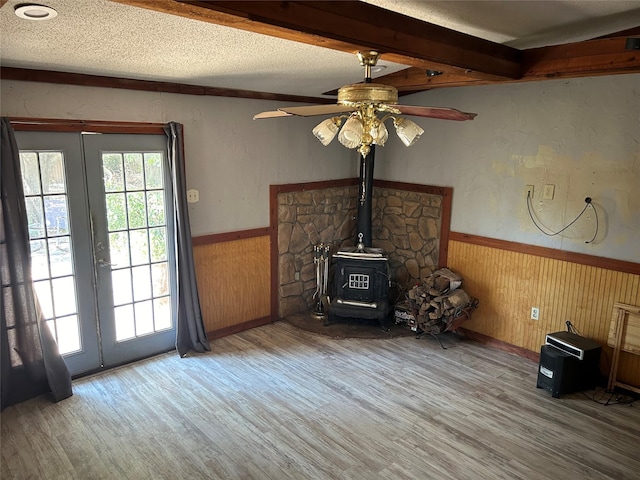 unfurnished living room with a wood stove, ceiling fan, french doors, light hardwood / wood-style floors, and a textured ceiling