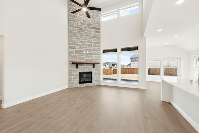 unfurnished living room with baseboards, ceiling fan, wood finished floors, a stone fireplace, and high vaulted ceiling