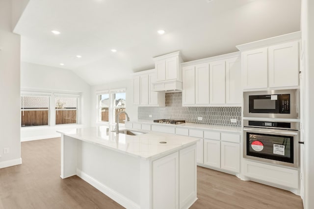 kitchen with lofted ceiling, a sink, appliances with stainless steel finishes, light wood-type flooring, and backsplash