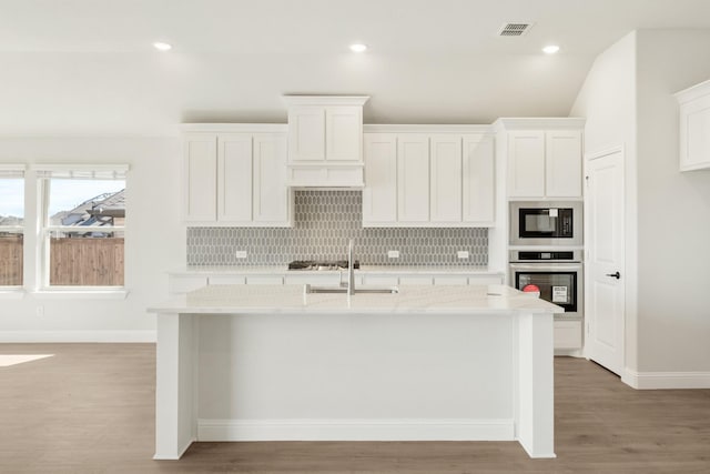 kitchen featuring visible vents, decorative backsplash, a sink, black microwave, and oven