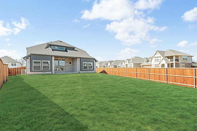 rear view of property featuring a fenced backyard, a residential view, central AC, and a yard