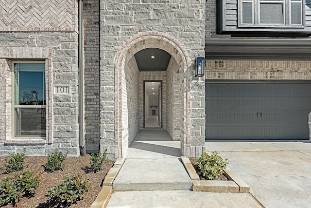 doorway to property featuring a garage, concrete driveway, and brick siding