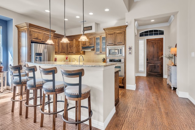 kitchen with dark wood-type flooring, decorative light fixtures, stainless steel appliances, light stone countertops, and decorative backsplash