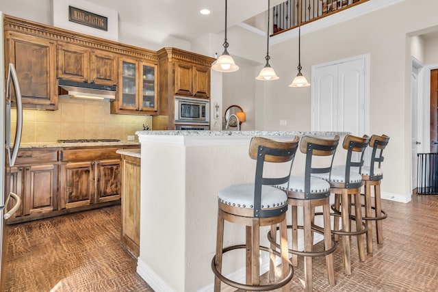 kitchen featuring appliances with stainless steel finishes, hanging light fixtures, tasteful backsplash, light stone countertops, and a kitchen island