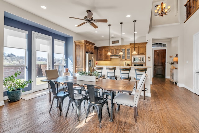 dining room with a towering ceiling, wood-type flooring, and ceiling fan with notable chandelier