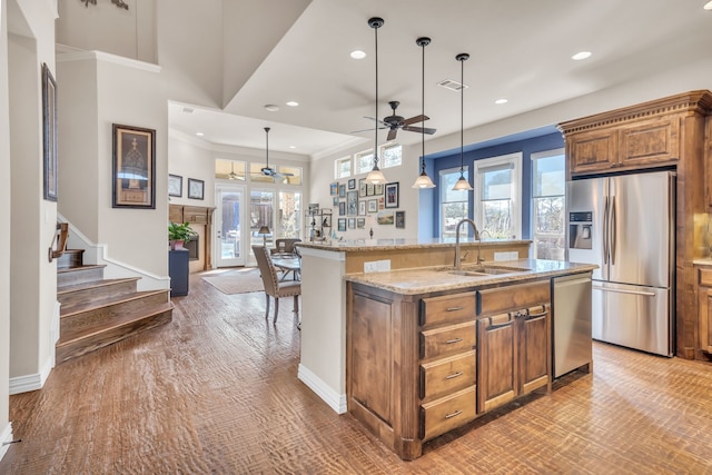 kitchen with pendant lighting, sink, a kitchen island with sink, stainless steel appliances, and light stone countertops