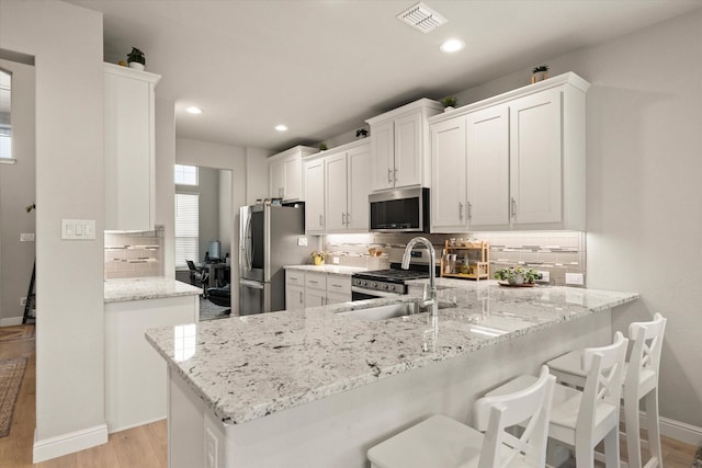 kitchen featuring white cabinets, sink, light stone countertops, appliances with stainless steel finishes, and kitchen peninsula