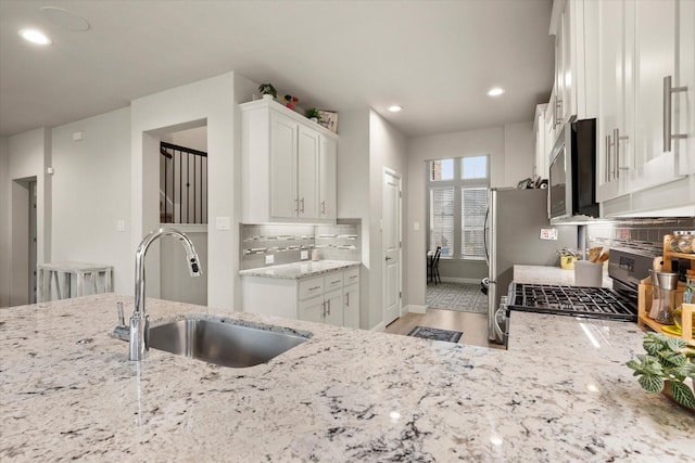 kitchen featuring decorative backsplash, appliances with stainless steel finishes, light stone counters, sink, and white cabinetry