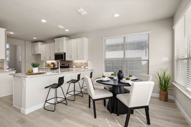 1504 Longspur Dr, Argyle, TX 76226 - kitchen featuring stainless steel microwave, a peninsula, white cabinetry, backsplash, and light wood-style floors