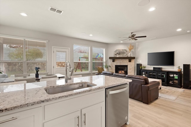 kitchen with dishwasher, white cabinets, sink, a fireplace, and light stone counters