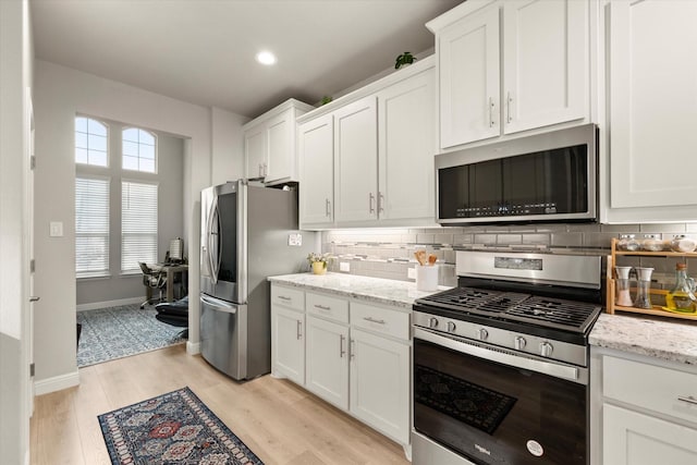 kitchen with backsplash, stainless steel appliances, white cabinetry, and light stone counters