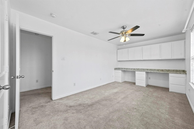 unfurnished bedroom featuring ceiling fan, light colored carpet, and built in desk