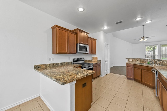 kitchen with kitchen peninsula, appliances with stainless steel finishes, ceiling fan, dark stone countertops, and light tile patterned flooring