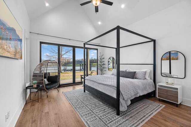 bedroom featuring ceiling fan, access to exterior, hardwood / wood-style floors, high vaulted ceiling, and a water view