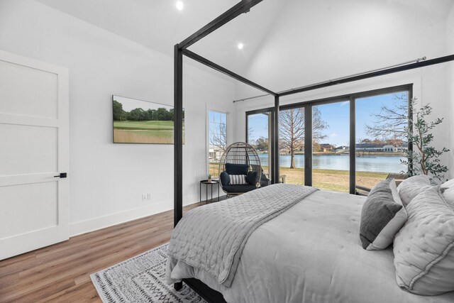 bedroom with vaulted ceiling, access to exterior, a water view, and hardwood / wood-style floors